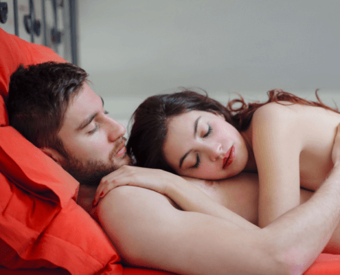 Loving husband and wife cuddling on red sheets - MarriageHeat