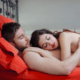 Loving husband and wife cuddling on red sheets - MarriageHeat