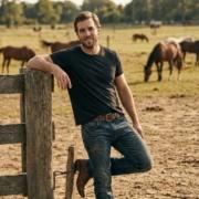 Handsome man leans against fence post on horse ranch ~ MarriageHeat